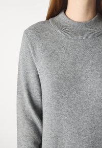 Maglione grigio lavorato a maglia con colletto alto a costine, tessuto testurizzato e maniche lunghe, caratterizzato da una finitura morbida e liscia.