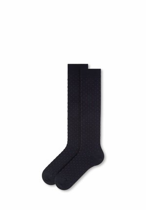Par de calcetines negros hasta la rodilla con pequeños lunares rojos, colocados planos con un calcetín ligeramente superpuesto sobre el otro.