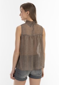 Bruine bloempatronen mouwloze blouse met een hoge gerimpelde halslijn en doorschijnende stof, gecombineerd met lichtgrijze shorts.