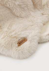 Produkt aus beigefarbenem Kunstpelz mit weicher Textur, versehen mit einem geprägten Lederetikett mit der Aufschrift "BARTS". Rundliche Form mit plüschigem Materialdesign.