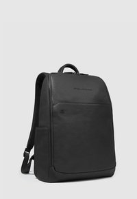 Zaino in pelle nera con texture liscia, chiusura con zip, tasca anteriore, spallacci imbottiti e logo sul davanti. Design minimalista e forma rettangolare.