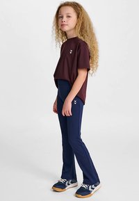 Vinröd t-shirt med korta ärmar och en vit logotyp, kombinerad med marinblå figurnära leggings. Uteskorna har en färgkombination av marinblått, vitt och beige.