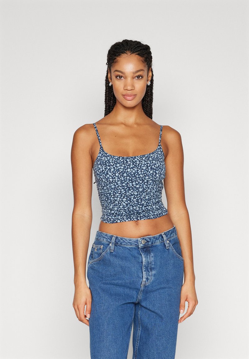 Top floral azul curto com alças finas, apresentando um design justo e textura plissada, combinado com jeans de cintura alta.