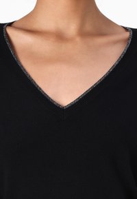 Maglione nero a V con una rifinitura metallica argento lungo il collo. Il tessuto appare liscio e tessuto, con una texture confortevole.