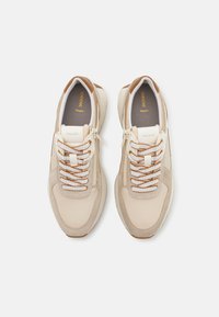 Beige und hellbraune Sneaker mit einer Mischung aus glatten und strukturierten Materialien, ausgestattet mit weißen Schnürsenkeln und einem dezenten Logo auf der Innensohle.
