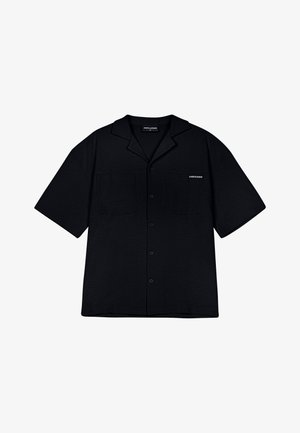 Melns īsām piedurknēm krekls ar teksturētu audumu, divām priekšējām kabatām un pogu aizdari. Iezīmēts ar apkakli un diskrētu logo detaļu.