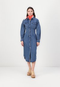 Jeans srajčna obleka v modri barvi s sprednjim gumbom, dvema žepoma na prsih in dolgimi rokavi. Ujemajo se s svetlimi klobuki in rdečim šalom z vzorcem.