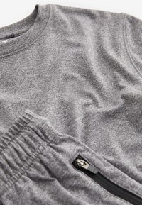 Mäkká sivá bavlnená košeľa a nohavice s elastickým pásom a detailom čierneho vrecka na zips.