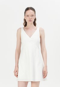 Bílá lněná šaty s výstřihem do V a širokými ramínky, mající přiléhavý živůtek a rozšířenou sukni, hladkou texturu a minimalistic design.