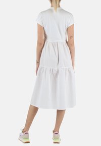 Abito di cotone bianco con maniche corte, vita arricciata e gonna a strati. Indossato con sneaker colorate con accenti rosa e verdi.