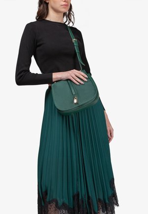 Borsa a tracolla verde realizzata in materiale liscio, con una patta con dettaglio di lucchetto dorato e una tracolla regolabile. La borsa ha una forma arrotondata.