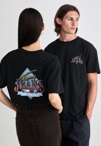 Tricouri negre din bumbac cu un grafic colorat "Tommy Jeans" pe spate, având un model rombic și textul "NEW YORK CITY".