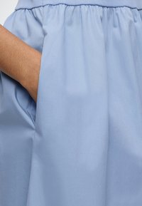 Main reposant dans la poche d'un vêtement bleu clair avec une ceinture élastique froncée.