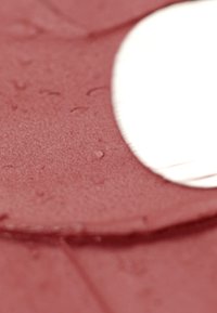 Silicone rosso morbido con una texture liscia, dotato di un accento circolare bianco. La superficie mostra lievi imperfezioni e una leggera lucentezza.