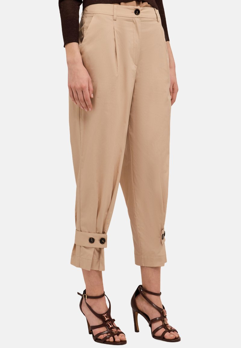 Beige beskurna byxor med veck, med knappar som dekorativ detalj vid mudden. Slät tygkvalitet med skräddarsydd passform, tillsammans med sandaler med höga klackar.