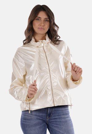 Giacca lucida di colore crema, con zip frontale, cordini e polsini elasticizzati. Design leggero e informale con una vestibilità rilassata.
