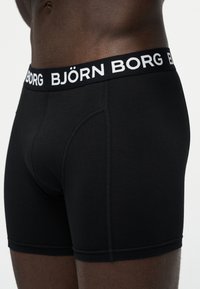 Μαύρα ανδρικά μποξεράκια με λογότυπο στη μέση που γράφει "BJÖRN BORG", φορεμένα σε κορμό άνδρα με σκουρόχρωμο δέρμα σε μονόχρωμο φόντο.