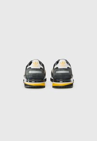 Black and grey athletic shoes with a yellow outsole, featuring a suede upper, reflective accents, and a white logo on the heel.