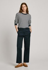 Jersey de rayas en azul marino y crema, combinado con pantalones de pierna ancha azul oscuro y zapatos planos marrones. Ajuste casual con puños acanalados.