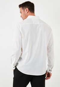 Camisa blanca de manga larga con acabado texturizado, cuello clásico y puños abotonados. Presenta un dobladillo curvado y una silueta entallada.