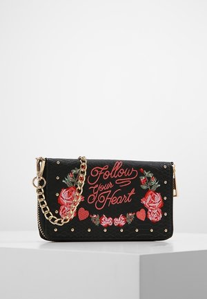 Pochette noire texturée avec chaîne dorée, roses rouges brodées, cœurs et texte « Suivez votre cœur » sur le rabat avant.