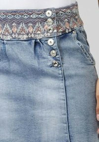 Jupe en denim de couleur bleu clair, avec une ceinture à motifs, cinq boutons décoratifs et deux poches latérales.