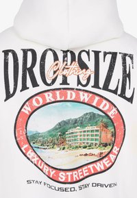 Weißer Hoodie mit dem Text "Dropsize Clothing Worldwide Luxury Streetwear" und einer Grafik eines Strandresorts mit Bergen und Palmen.