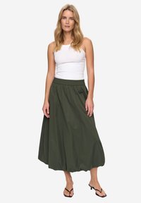 Ciemnozielona spódnica do kolan z elastycznym paskiem w talii i luźnym, zwiewnym materiałem. Noszona z białym topem na ramiączkach i czarnymi sandałami.