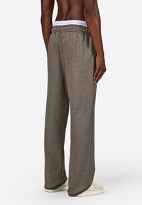 Hnedé, textúrované nohavice s širokými nohavicami a čiernym pásom, s jemnými vertikálnymi pruhmi, ktoré majú uvoľnený strih a postranné švy.