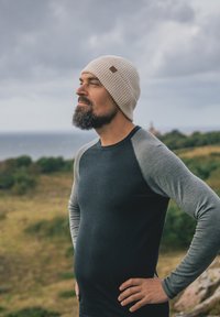 Light beige knitted beanie with a small logo tag. Dark gray long-sleeve shirt with contrasting light gray sleeves, fitted shape, and crew neckline.