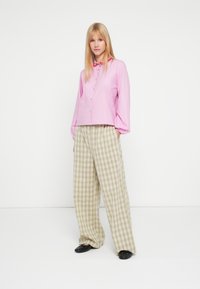 Rózsaszín galléros ing, bő, kockás mintás világoszöld és bézs nadrággal párosítva. A modell fekete lapos cipőt visel.