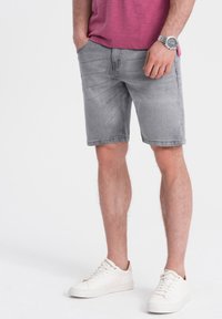 Pantalones cortos de mezclilla gris con un corte recto, bolsillos delanteros y un acabado ligeramente desgastado, combinados con zapatillas blancas.