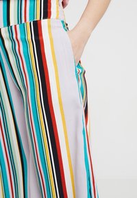 Striped trousers in shades of turquoise, red, black, and yellow. Made from smooth fabric with side pockets and a relaxed fit.