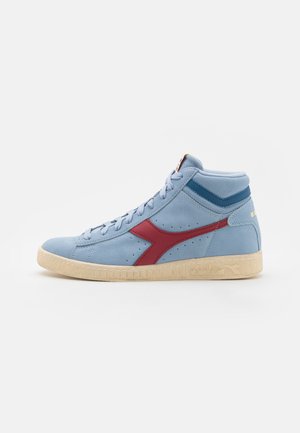 Baskets montantes en daim bleu clair avec des accents rouges, surface texturée et une semelle en caoutchouc crème ornée d'un logo et de détails perforés.