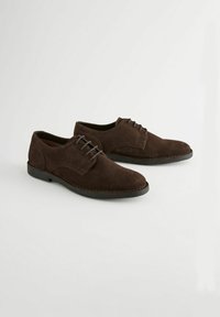 Zapatos de ante marrón con cordones, con punta redondeada, detalles de costura sutiles y suela de goma negra. Textura suave con un diseño clásico.