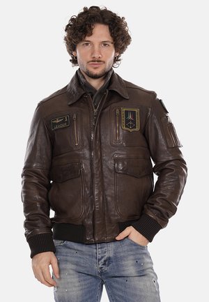 Giubbotto bomber in pelle marrone con polsini e fondo a coste, dotato di quattro tasche e toppe in stile militare sul petto e sulla manica.