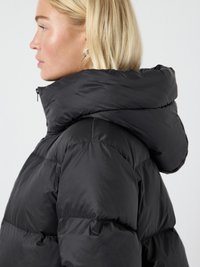 Chaqueta de plumas negra con un cuello alto y una gran capucha. La tela parece brillante y acolchada, con secciones voluminosas y rellenas.