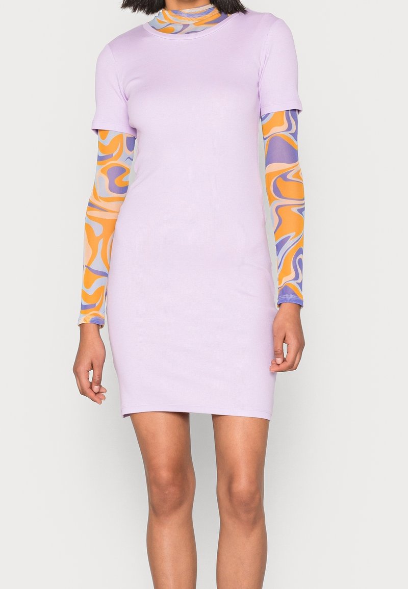 Robe ajustée lilas à manches courtes, portée par-dessus un haut à manches longues avec des motifs abstraits orange et violet. Texture de tissu lisse.