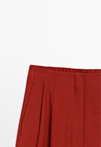 Pleated rust-colored skirt with a waistband, made from fabric with a textured finish. Visible stitching and side pockets.