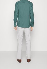 Zielona longsleeve z zaokrąglonym dołem, w połączeniu z jasnoszarymi spodniami. Brązowe skórzane buty dopełniają stylizację. Spodnie mają prosty krój.
