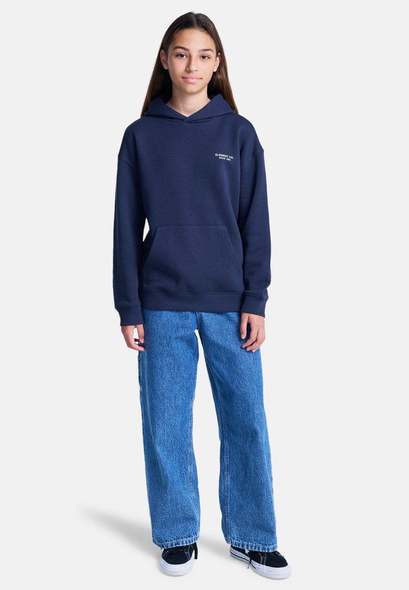 Sudadera con capucha azul marino, con bolsillo frontal y detalle de logo blanco, combinada con jeans de pierna ancha azul claro y zapatillas negras.
