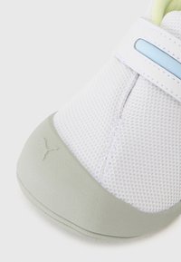 Baskets en mesh blanches avec une semelle en caoutchouc grise, comprenant un accent bleu clair et une sangle Velcro. Tige texturée avec des détails de couture.