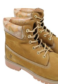 Botas de tobillo de ante marrón con un puño texturizado con un patrón de mapa, ojales dorados y costuras en contraste sobre una suela de goma.