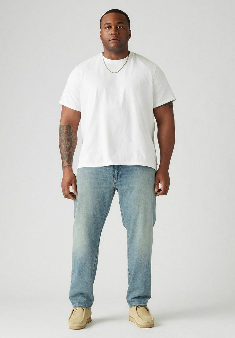 T-shirt en coton blanc, coupe décontractée, associé à un jean bleu clair. Des chaussures beiges complètent la tenue. Design simple, sans motifs visibles.