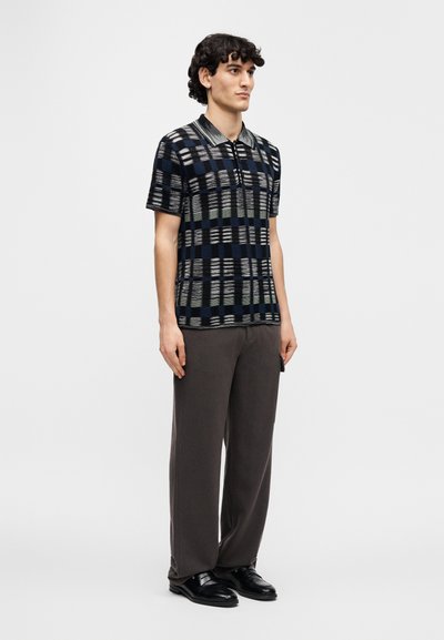 Short-sleeve polo shirt with a geometric pattern in navy, light blue, and gray. Worn with loose gray trousers and black leather shoes.