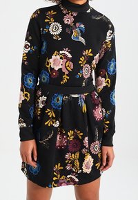 Svart långärmad klänning med en färgglad blommönster i rosa, blått och gult, med en figursydd överdel och utsvängd kjoldetalj.