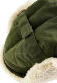 Tissu en olive matelassé avec une doublure en fausse fourrure crème douce. Dispose d'une sangle en tissu pour un maintien sécurisé. Détails de surface texturée présents.
