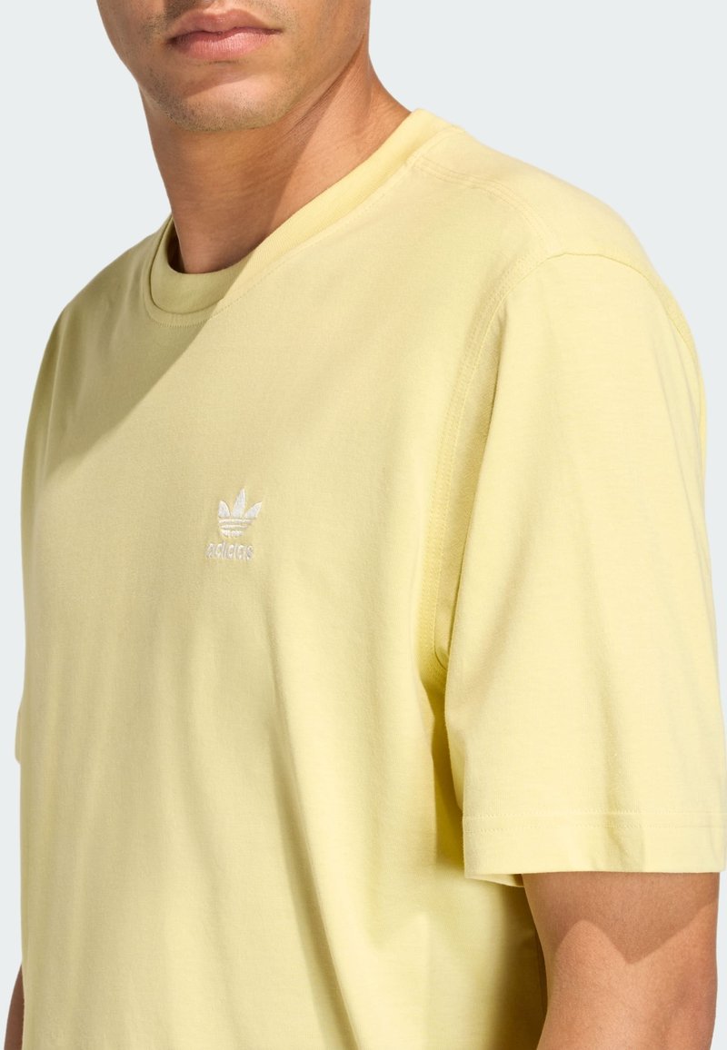 Light yellow cotton t-shirt with a crew neck, short sleeves, and a small white embroidered logo on the chest. Soft texture, relaxed fit.