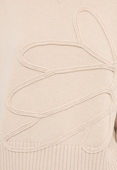 Pull beige avec un design texturé présentant un motif de contour surélevé. Le matériau est tricoté, avec des accents en bord-côte.