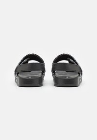 Černé sandály s dvojitými popruhy s texturovaným povrchem, plochou podrážkou a vzorovaným okrajem.